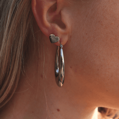 Model wears heart shaped stainless steel studs with PĀMU logo engraved and stainless steel large hoop earrings